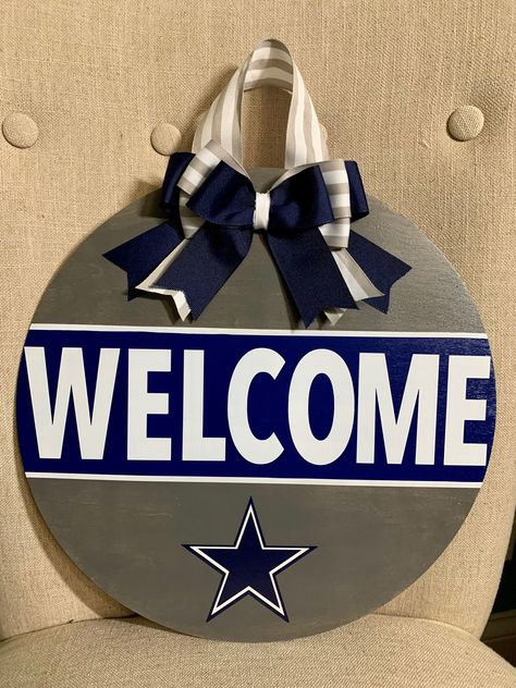 "Show your pride with this Cowboys Door Hanger! Just in time for the Playoffs!  Ready to hang, this is a 14\" wood round, hand painted with layered vinyl lettering and decor.  Coated with 2 layers of Polycrylic finish.  Ribbon and greenery may vary based on availability but will closely resemble the pictured.  If you would like to modify colors/decor/team name, feel free to message us!" Cowboys Door Hanger, Dallas Cowboy Door Hanger, Dallas Cowboys Front Porch Sign, Dallas Cowboys Door Hanger, Nfl Door Hanger, Dallas Cowboys Round Wood Door Hanger, Dallas Cowboys Signs Wood, Dallas Cowboys Round Wood Sign, Cowboys Wood Door Sign