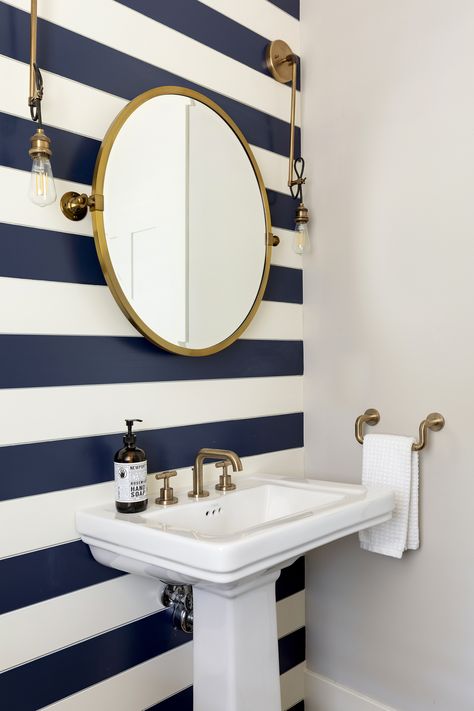 Statement wall with the gold fixtures and gold finished mirror gives off an elegant lakehouse feel. Love the simplicity combined with a fun pattern. Striped Bathroom Walls, Blue Vanity Bathroom, Coastal Powder Room, Nautical Interior Design, Navy Bathroom, Nautical Interior, Blue Accent Walls, Nautical Bathroom Decor, Blue Vanity