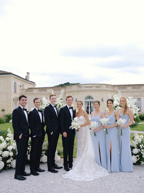 Bridal party photo with bride, groom, bridesmaids in light blue dresses, and groomsmen in black suits with black bow ties, set against the elegant Chateau Gassies. Black Tux With Light Blue Tie, Bridal Party Color Palette, Black And Light Blue Wedding, French Blue Wedding Color Palettes, Light Blue Bridal Party, Blue Bridesmaid Dresses With Groomsmen, Light Blue And Black Wedding, Chateau Gassies, French Blue Bridesmaid Dresses