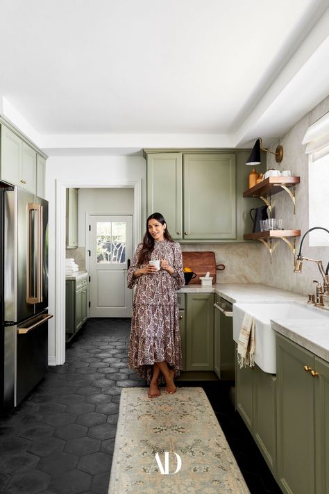 Actor Freida Pinto in the other half of the kitchen, which includes Bobby Berk’s sage green cabinetry and a fridge by GE Café Appliances. The renovated kitchen also features finishings by Brizo and leather tiling by Walker Zanger. The oriental rug adds an extra layer of warmth to the space and ties the room together with its reflection of the backsplash coloring. #kitchen #greenkitchen #greencabinets #blacktiles #rug #backsplash #sink #window #openshelving #fridge #californiahome #whitewalls Bobby Berk, Traditional Eclectic, Kitchen Breakfast Nooks, Walnut Shelves, Freida Pinto, Casa Vintage, Kitchen Paint Colors, Los Angeles Homes, Kitchen Paint