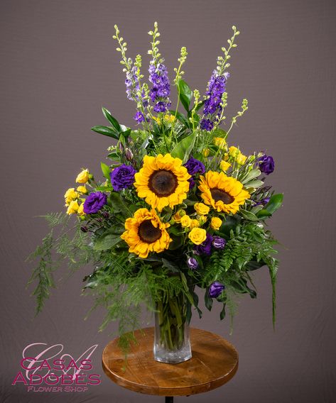 This Enduring Love Vase is designed with sunflowers, purple larkspur, purple lisianthus and yellow spray roses ina d beautiful vase. Sunflower Cemetery Arrangements, Sunflower And Purple Flower Arrangements, Purple And Gold Floral Arrangements, Purple And Yellow Floral Arrangement, Fall Altar Flowers, Purple And Gold Flower Arrangements, Floral Arrangements In Vases, Yellow And Purple Flower Arrangements, Sunflower Bouquet Vase