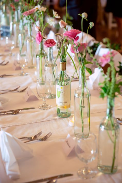 Wine Bottle Vases Centerpiece, Wine Bottle Centerpieces With Flowers, Simple Wine Bottle Centerpieces, Wine Bottles With Flowers, Glass Bottle Flower Arrangements, Diy Bridgerton Decor, Wine Bottle Vase Flowers, Flower In Wine Bottle, Petals And Prosecco Centerpieces