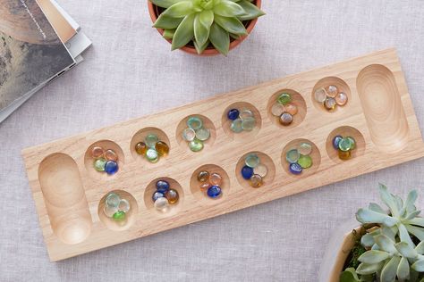 A profile of the ancient board game Mancala, this count-and-capture game has variations worldwide, but its Arabic name gives a clue as to its origin. Mancala Game, Stone Game, Game Template, Bags Game, Activity Kits, Ric Rac, Critical Thinking Skills, Strategy Games, Game Board