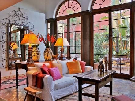 From the terra-cotta tile flooring to the tall arched French doors, this living room is a contemporary twist on traditional Spanish design. The warm accent colors look crisp against the white walls and sofa. The living room's color scheme is carried through to the adjacent traditional Spanish-style courtyard. Design by Carole Meyer Contemporary Mexican Interior Design, Mexican Living Room, Spanish Living Room, Modern Mexican Home Decor, Spanish Interior Design, French Style Living Room, Modern Mexican Home, Mexican Interior Design, Pintu Interior