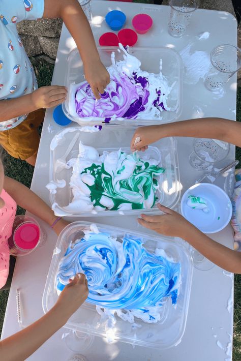 Children’s hands stirring blue and green liquid watercolors into white shaving cream, creating a swirling pattern during a sensory activity. Christmas Shaving Cream Activities, Shaving Cream Play, Shaving Cream Sensory Play, Shaving Cream Activities, Shaving Cream And Food Coloring, Potions For Kids, Shaving Cream Art, Shaving Cream Painting, Sensory Activities For Preschoolers