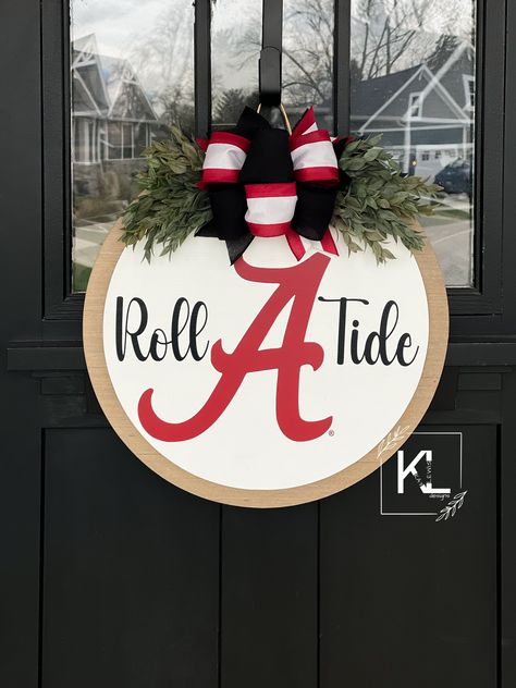 "*OFFICIALLY LICENSED COLLEGIATE PRODUCT* Alabama Crimson Tide Door Hanger | Alabama Roll Tide | Alabama Door Hanger | Alabama Wreath | Roll Tide Wreath | University of Alabama This sign comes in  sizes 16\", 18\", 20\" & 22\". Comes ready to hang with twine wire attached! One coat of poly acrylic applied! Bow and greenery attached! (NO glue used) All signs are handmade from myself and my husband!  From hand cutting the circle shapes, to hand making the bows, to hand painting your door hanger. P Roll Tide Door Hanger, Crimson Tide Decor, Fall Hanger, Alabama Football Wreath, Alabama Door Hanger, Alabama Crafts, Alabama Wreaths, Painted Chair, Wooden Door Signs