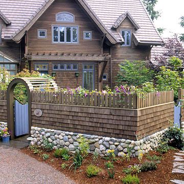 Combination Fieldstone and Wood Fence. If you love the look of stone and wood fencing, why not enjoy both? This fence features a low fieldstone wall topped with a wooden shake center and crowned with small pickets. A stone foundation makes the fence look solid and substantial. Round fieldstones are usually mortared into place because of their shape. Stone Wall Privacy Fence, Wood Fence With Stone Columns, Rock And Wood Fence, Stone Wall Outdoor Fence, Fieldstone Wall, Decorative Fencing, Picket Fencing, Stone Foundation, Stone Walls Garden