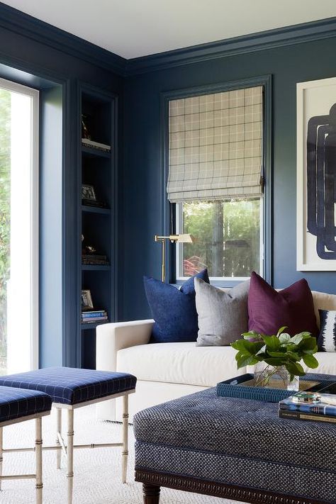 Navy blue molding line navy blue home office walls framing a built in navy blue recessed shelf positioned adjacent to a window dressed in a gray check roman shade. Moody Blue Living Room, Home Office With Daybed, Office With Daybed, Blue Home Offices, Den Library, Transitional Family Room, Contemporary Family Room, Family Room Inspiration, Library Office