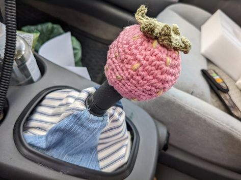 A gear shift is shown in a gray car, the cloth boot cover is alternating blue jeans fabric and Blue and white striped fabric. The round gear knob has a crocheted cover, it is shaped as strawberry and is light pink with yellow seeds and green leaves on top. Car Shift Cover, Diy Crochet Car Accessories, Chevy Car Accessories, Crochet Stick Shift Cover, Crochet Car Shifter Cover, Cute Car Themes, Crochet Car Gear Shift Cover, Skullcandy Crusher Evo Aesthetic, Crochet Car Accessories Ideas