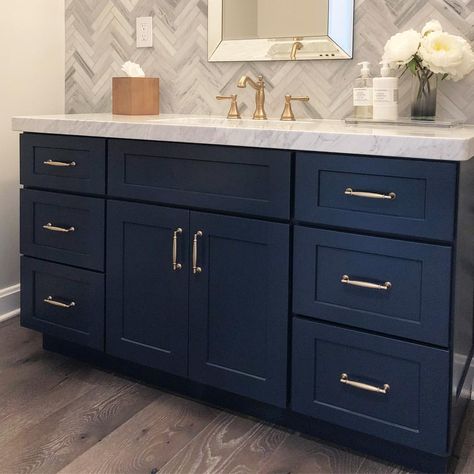 What’s not to love about this stunning powder room!? The blue vanity cabinet pairs so perfectly with the satin brass hardware. The tile wall in the chevron pattern is trendy but the neutral grey palette is very versatile. #bathroom #bathroomdesign #bathroomremodel #powderroom #interiordesign #remodel #interior #designer #interiordesigner #blue #bluecabinets #bluebathroom #homedesign Bathroom Tile Ideas With Blue Cabinets, Navy And Grey Bathroom Decor Ideas, Dark Blue Wall Bathroom, Blue And Tan Bathroom, Blue And Gold Bathroom, Boys Bathroom Ideas, Bathroom Update Ideas, Tan Bathroom, Blue Bathrooms