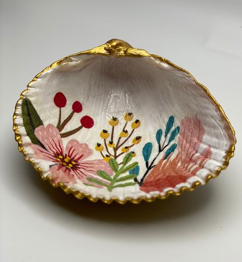 "Our cockle shell holders are a lovely way to store your jewelry or trinkets. Each shell is gently cleaned by hand to maintain the uniqueness of each shell. Your shell is then handpainted, decoupaged, trimmed and backed with gold leaf paint, and covered with gloss varnish.  The shell dish is a lovely accent piece for the home and makes a perfect hostess gift, favor, or decoration.  This dish is available in 3.5\" x 3.5\" or 2.5\" x 2.5\".  You can select to have an optional base added to the shell for an additional charge. Please note: Each shell is found on Oak Island, North Carolina and lovingly selected for you. The shells have been tumbled by the ocean and will have natural imperfections that make each one unique." Painted Shell Ideas, Hand Painted Seashells, Seashell Diys, Diy Seashell Crafts, Shell Jewelry Holder, Painted Sea Shells, Painting Shells, Oak Island North Carolina, Decoupage Shells