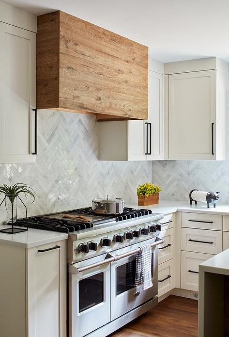 White and gray marble herringbone wall tiles hold a reclaimed wood range hood between white shaker upper cabinets finished with oil rubbed bronze pulls. Reclaimed Cabinets, Herringbone Wall Tile, Backsplash White, Farm Style Kitchen, Kitchen Hood Design, Marble Herringbone, Tiles Backsplash, Herringbone Wall, Reclaimed Wood Kitchen