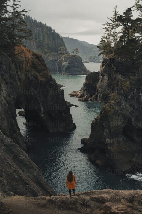 by Ammar Habib | Available to license on stills.com Cliff By The Sea, Standing On The Edge, Edge Of A Cliff, Rocky Cliff, Calm Sea, Orange Coat, Conifer Trees, Coat Stands, Cloudy Day