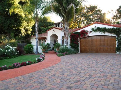 This Spanish Colonial Revival house with a barrel tile roof features a paver driveway, sidewalk and a wooden, arched garage door surrounded by bougainvillea. A mission parapet on top of the roof adds to the home's eclectic look. Colonial Revival House, Spanish Style Decor, Spanish Colonial Homes, Mediterranean Exterior, Spanish Decor, Mediterranean Style Homes, Mediterranean Home Decor, Spanish Style Home, Casas Coloniales