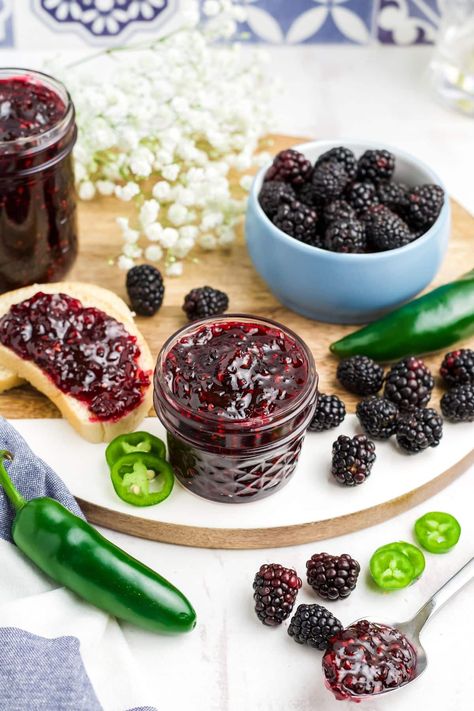 Blackberry jalapeno jam in a jar with some spread on a toast to the side and fresh berries around on the table.