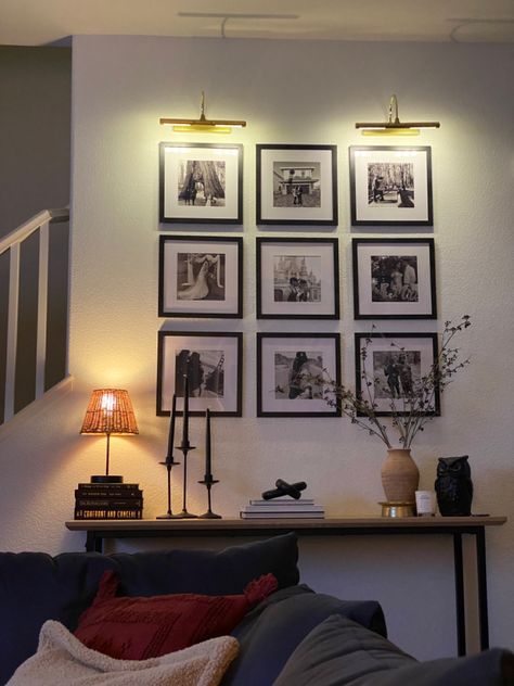 Black frame gallery wall with wooden console table and gold picture lights, transitional design entryway Black Frame Gallery Wall Hallways, Hall Wall Picture Ideas, Entryway Picture Wall Ideas Modern, Gallery Wall With Table Under, Accent Wall Photo Gallery, Gallery Wall On Slanted Wall, Console Table Lighting, Black Square Picture Frames, Gallery Wall With Console Table