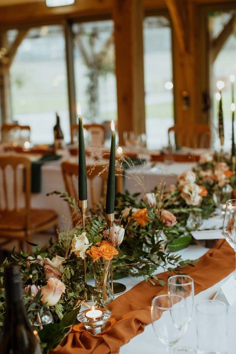 Burnt orange wedding tablerunner, forest green wedding napkins, forest green tapered candles and bottles of wine with suspended foliage and fairy lights decor at wedding | Jessica Grace Photography Terracotta And Green Centerpieces, Green And Burnt Orange Wedding Theme, Dark Orange And Sage Green Wedding, Burnt Orange Table Runner Wedding, Sage Green And Burnt Orange Wedding Bouquet, Centerpieces Wedding Burnt Orange, Burnt Orange Centrepiece, Green White Burnt Orange Wedding, Green And Orange Wedding Table Decor