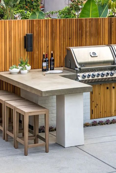 A modern outdoor bbq area with a large tiled unit with a grill, a concrete countertop, wooden stools and potted greenery Outdoor Kitchen Design Layout Grill Area, Outdoor Kitchen Design Modern, Outdoor Bbq Area, Outdoor Grill Station, Outdoor Barbeque, Kitchen Design Layout, Kitchen Design Diy, Outdoor Kitchen Plans, Outdoor Bbq Kitchen