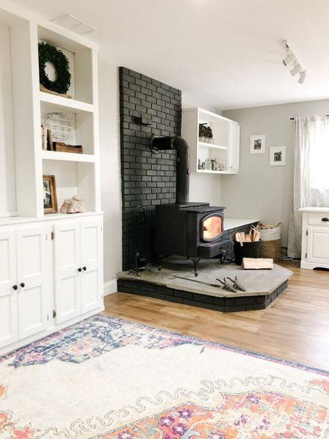 When we moved in to our home, the wood stove brick surround was RED. Just like the room..So when we painted the room it’s first color I wanted to tone down the red in the brick by white washing it. I thought it looked great and it was really easy. You can see how I did it here. While I am updating our family room downstairs, and the built-ins are now finished, I have been been eyeing the brick again. I had thought about painting it dark, doing another coat of white wash or simply p… Family Room With Wood Burning Fireplace, Painting Brick Woodstove Surround, White Wash Brick Wood Stove, What Color To Paint Brick Fireplace, Wood Stove Update, Finished Basement Ideas With Woodstove, Painted Brick Wood Stove Surround, Stove Brick Surround, Wood Stove Makeover