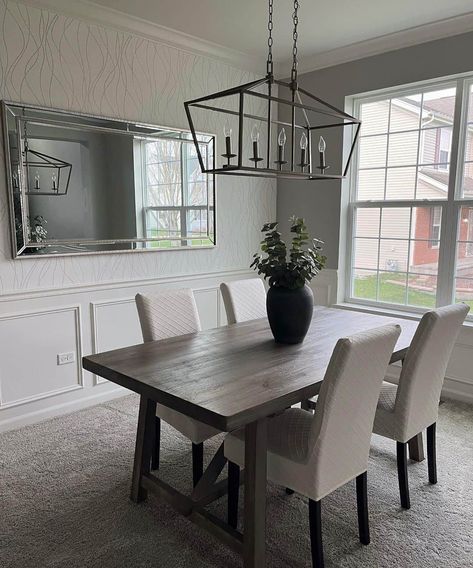 A black metal linear lantern light is hung above a stained wood rectangular modern farmhouse dining table. The table is paired with off-white upholstered dining chairs. Make any room look bigger with a stunning beveled mirror mounted to the wall. Farmhouse Dining Tables, Light Wood Dining Table, Rectangle Dining Room Table, Modern Farmhouse Dining Table, Room Look Bigger, Lounge Rooms, Stylish Dining Room, Modern Farmhouse Dining, White Dining Room