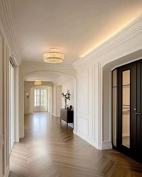 A long hallway with white walls, arched doorways, and crown molding. The floor is hardwood and there is a console table with a vase in the middle. Hallway With Molding, White Crown Molding, Arch Moulding, Crown Molding Ideas, Stunning Hallway, Elegant Hallway, Herringbone Hardwood Floors, Arched Doorways, Arch Molding