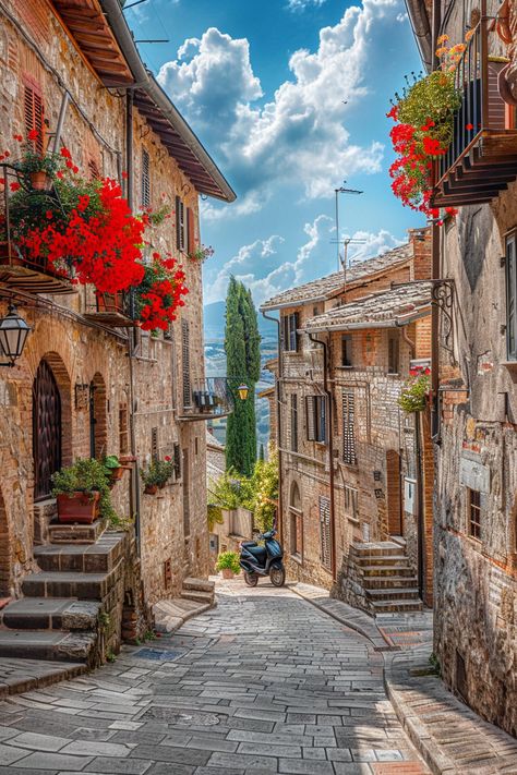 Cobblestoned street in San Gimignano, Italy with red flowers and vintage architecture under clear blue sky Italy Places Aesthetic, Italy Cobblestone Streets, Narrow Streets Italy, Italian Neighborhood Aesthetic, Old Italian Architecture, Italian Buildings Architecture, Italy Buildings, Architecture In Italy, Italy Town