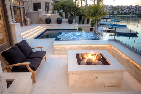 A fire pit surrounded by seating creates a cozy spot to relax beside this breathtaking lakefront view. The infinity-edge pool and hot tub are surrounded by square glass tiles, which draw the eye and create a colorful focal point in the neutral space. Moderne Pools, Fire Pit Materials, Infinity Pools, Pool Water Features, Contemporary Patio, Backyard Fireplace, Storage Inspiration, Backyard Pool Designs, Swimming Pool Designs