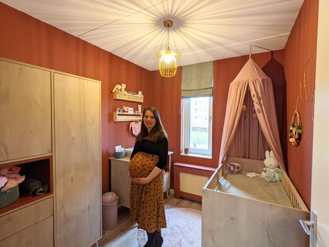 Babykamer met terracotta muur, roze en groene accessoires en natuurlijke meubels Pins