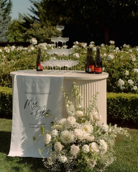 This might just be the dream summer wedding set up ✨ Add an extra special touch to your welcome sign by combining it with an elegant drinks station. I fell in love with this beautiful display at @campdavidfarm, featuring natural linen and a tonal floral arrangement. Pairing your welcome sign with a drinks station creates a warm, elegant welcome for your guests. Opting for a tonal colour scheme keeps everything seamless and sophisticated. Follow for more luxury wedding inspiration 💍 ✨ ... Welcome Drinks Table, Florals On Bar Wedding, Wedding Welcome Table Ideas, Floral Wedding Signage, Signage Florals, Elegant Drinks, Fabric Signage, Wedding Bar Floral Installation, Drinks Station