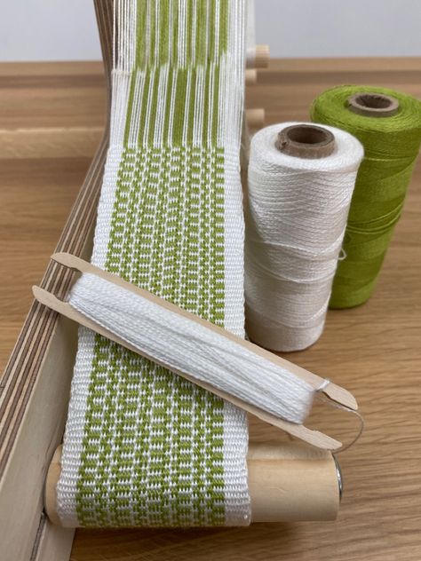 Green and white weaving on an Inkleloom Inkle Loom Weaving Patterns, Inkle Weaving Patterns For Beginners, Inkle Loom Patterns Free, Inkle Loom Weaving, Inkle Weaving Patterns Free, Inkle Loom Patterns For Beginners, Inkle Loom Patterns, Loom Tools, Inkle Weaving Patterns