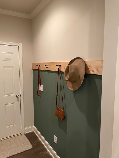 Green accent wall in entryway hallway/mud room with coat hangers and natural wood accent. Boho Green Accent Wall, Sage Green Entryway Wall Colors, Black White And Green Entryway, Pine Green Accent Wall, Mudroom Accent Wall Ideas, Green Accent Wall Hallway, Accent Wall With Hooks Entryway, Entrance Accent Wall Ideas, Green Mudroom Walls