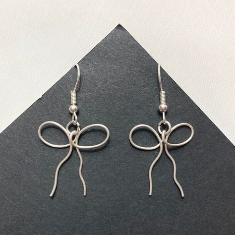 ✦ Dainty ribbon/bow earrings that will meet your coquette, dollcore, and balletcore needs!  ✦ New & handmade ✦ Handle with delicacy to avoid bending the wire! ✦ Imperfections & plier marks may be visible ✦ Silver/gold plated lead & nickel free zinc alloy hooks; 20 gauge wire ✦ Rubber backings included ✦ More jewelry on my shop; message for customs! Wire Keychain Ideas, Silver Wire Earrings Handmade, Handmade Wire Earrings Ideas, Wire Earing Tutorials, Simple Wire Pendant, Wire Shapes For Jewelry, Cute Wire Earrings, Goth Wire Jewelry, Metal Wire Earrings