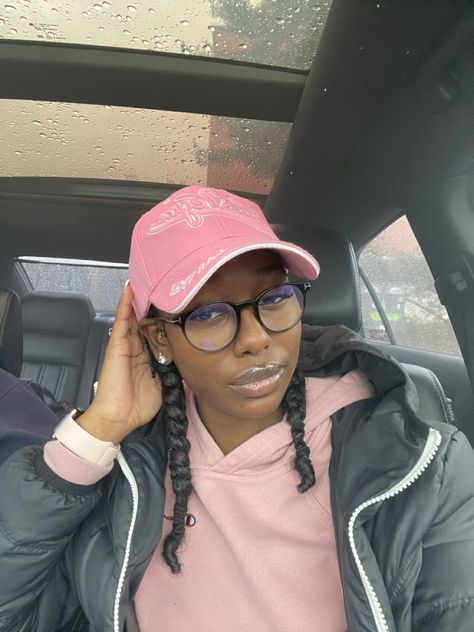 She has curly hair braided into two braids. She is sitting in car wearing a pink hoodie and pink baseball cap. Visor Hat Hairstyles Black Women, Hairstyles With Hats Black Women, Natural Hairstyles With Hats, Braids With A Hat Black Women, Natural Hairstyles With Beanie, Cap With Braids Black Women, Baseball Hat Curly Hairstyles, Hats And Braids Black Women, Curly Hairstyles For Hats