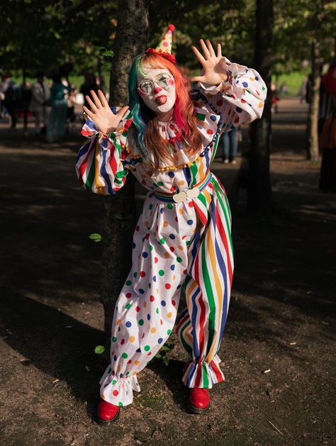 Girl in a white clown suit, half spotty, half stripey with primary colours. She has rainbow hair and a little hat and red shoes Make Your Own Clown Costume, Clowncore Halloween Costumes, Clown Outfit Reference, Clowncore Outfit Drawing, How To Make Clown Costume, Clown Outfit Inspiration, Clown Halloween Costumes Cute, Cute Clown Costume Halloween, Rainbow Clown Outfit