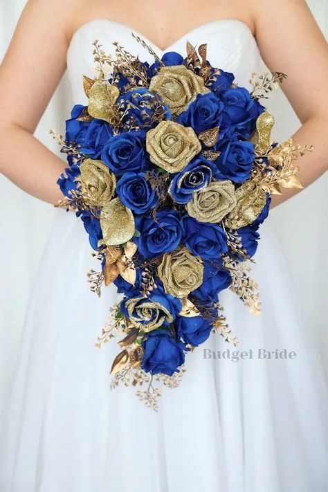 cascading brides bouquet with royal blue roses and gold glitter tipped horison blue roses, gold glitter calla lillies and gold glitter roses. accented with gold fern and gold leaves Blue And Gold Flower Bouquet, Dark Blue And Gold Wedding Theme, Blue And Gold Wedding Bouquet, Royal Blue And Rose Gold Wedding, Royal Blue Gold And White Wedding, Royal Blue And Gold Wedding Theme, Royal Blue Beach Wedding, Royal Blue Weddings, Wedding Color Royal Blue