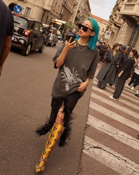 Young Asian woman with blue medium length hair, wearing a gray oversized t shirt, midi black skirt with feather trim and yellow knee-length snake skin boots China Street Style, Margaret Zhang, China Street, Editor In Chief, Vogue China, Rich Man, Spring 2024, Milan Fashion, Fashion Week Spring