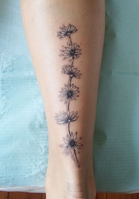 Daisy tattoo on the back of the calf Sunflower Tattoo On Calf, Daisy Tattoo On Leg, Pretty Calf Tattoos For Women, Calf Tats For Women, Sunflower Chain Tattoo, Daisy Leg Tattoos For Women, Daisy Chain Tattoo Arm, Daisy Foot Tattoos For Women, Daisy Leg Tattoo