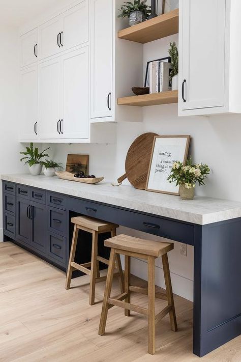 Kitchen features a blue desk with wooden sawhorse stools, oak floating shelves flanked by white upper cabinets accented with bronze pulls, blue lower cabinets topped with white quartz counters and bronze pulls and light wooden floors. White Upper Cabinets, Pure Salt Interiors, Light Wooden Floor, Oak Floating Shelves, Kitchen Desks, Pure Salt, White Shiplap Wall, Blue Dining Chair, Blue Kitchen Cabinets