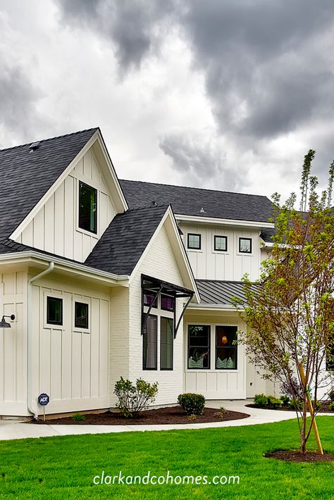 The Heartland. Board and batten siding is painted a creamy white that contrasts with the black windows and metal awnings. #modernfarmhouse #whitehouse #boardandbatten #customhome #blackwindows Modern Farmhouse Awnings Over Windows, Cream Exterior Black Windows, Farmhouse Roof Styles, Brick House Metal Roof, Farmhouse Awnings Over Windows, Farmhouse Windows Exterior, Metal And Shingle Roof Combination, Magnolia Homes Exterior, Awnings For Windows