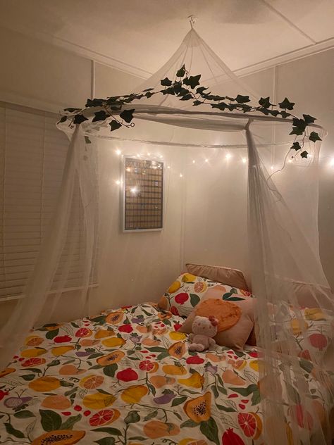 White room with queen bed. Peach themed quilt cover with a white canopy on top with vines and soft yellow lights. Pink Bed Canopy Aesthetic, Cottage Core Canopy Bed, Above Bed Canopy, Bed With Canopy Aesthetic, Corner Bed Canopy Ideas, Corner Canopy Bed, Bed Canopy Aesthetic, Corner Bed Canopy, Curtains Above Bed