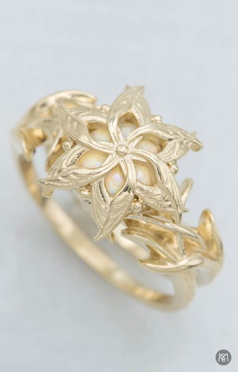 This gold engagement ring was inspired by Nenya, an elvish ring of power worn by Galadriel in the Lord of the Rings. The design we created for this customer sets a white opal under yellow gold flower detail to blend her love for the trilogy and for the unique look of opal. The unique styling of this design also provides a layer of protection for the softer opal. Nenya Ring Galadriel, Elvish Wedding Rings, Lord Of The Rings Engagement Ring, Nenya Ring, Galadriel Ring, Galadriel Rings Of Power, Lord Of The Rings Jewelry, Nerdy Engagement Rings, Elvish Ring