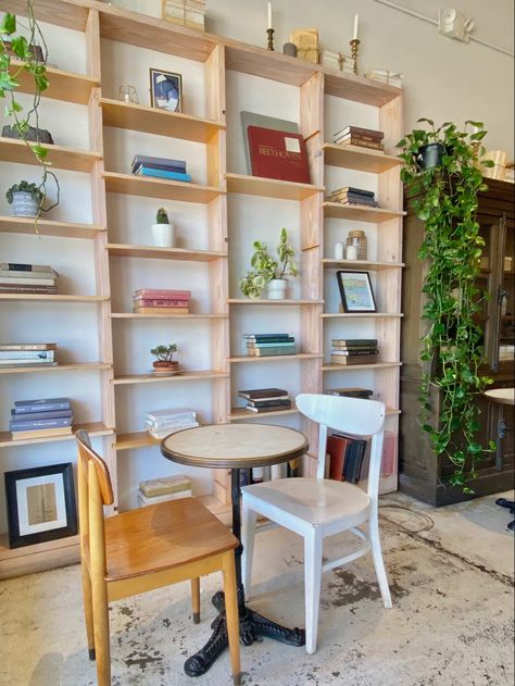 floor to ceiling shelf filled with books and greenery/ plants in a coffee shop Cafe Shelf Decor, Coffee Shop Bookcase, Book Shelf In Cafe, Opening A Bookstore Coffee Shop, Hanging Greenery Coffee Shop, Ceiling Shelf, Aesthetic Bookstore, Greenery Plants, Ceiling Shelves