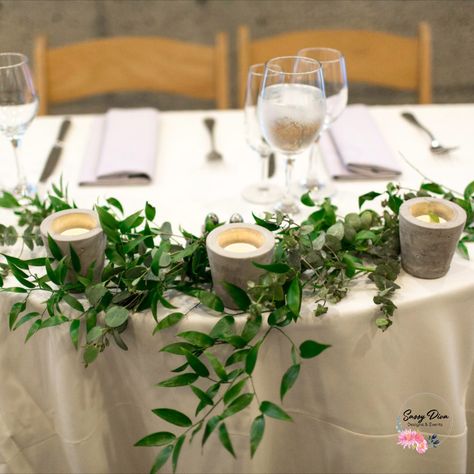 Sometimes all you need is a simple decoration added to your Sweetheart Table! This couple opted for some Italian Ruscus, Silver Dollar Eucalyptus, and Cement Tealight candle holders.   #weddingflorist #bayareaflorist #bayareawedding #bayareaweddingflorist #weddingflowers #sweethearttable #sweetheartarrangement #headtablearrangement #headtable #candle #weddingcandles #greenery #simplewedding #simple #greenandwhite #greenandwhitewedding  PC: Katheryn Lewis Photography Sweetheart Table Wedding Eucalyptus, Sweetheart Table Greenery Simple, Eucalyptus Runner With Candles, Top Table Greenery Garland Wedding, Sweetheart Table Simple, Sweetheart Table Greenery, Greenery And Candle Table Runner, Wedding Eucalyptus Floral Table Garland, Flowers Sweetheart Table