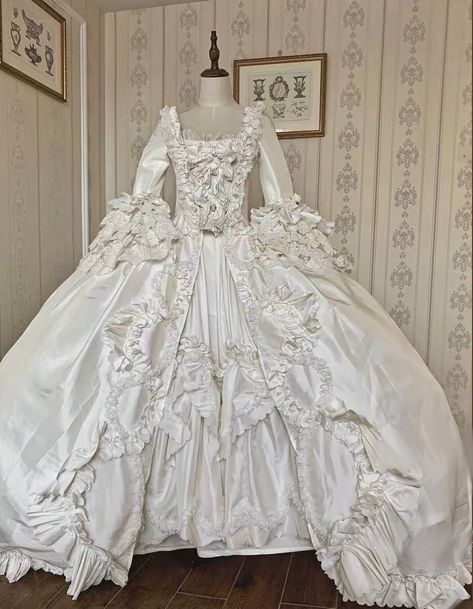 This stunning Luxury Antique Baroque Style Satin Wedding Dress with Floral Long Sleeves is the perfect choice for the bride who wants to make a statement on her special day. This 1800 ball gown features a beautiful baroque-inspired design with intricate details and luxurious satin fabric. The bodice is fitted with a sweetheart neckline, and the long sleeves are adorned with delicate floral appliques. The skirt is full and voluminous, with a sweeping train that adds a dramatic touch. This dress i 1700 Wedding Dress, White Rococo Dress, Georgian Wedding Dress, Victorian Era Wedding Dress, Ball Gown Wedding Dress With Sleeves, 17th Century Wedding Dress, 1700s Wedding Dress, Versailles Costumes, 1800 Wedding Dress