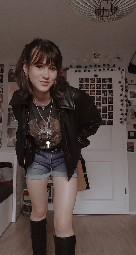 A girl standing in her room in shorts, a queen T-shirt, leather jacked, leather boots and a white cross-neckless 50s Fashion Rock N Roll, 90 Rock Outfit, Outfits For A Gig, Old Rock Concert Outfit, Cool Rock Outfits, Female Rockstar Outfit 80s, Rock Band T Shirts Outfits Women, 80s Rock Women Outfits, 80s Rockstar Gf Outfits