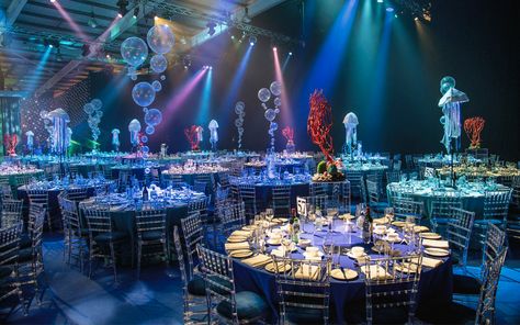 To access the dining area guests made their way through an opulent deep wall of fabric columns, emulating waves and shafts of light in the sea. Dining tables were dressed in four different shades of blue cloths, surrounded with clear perspex chairs. Bubble, coral and internally illuminated jelly fish table centres combined with creative under the sea lighting brought the space to life and left guests utterly in awe as 3mtr jellyfish acrobats danced the night away over the top of the tables. Under The Sea Gala, Explore Images, Sea Wedding Theme, Grad Dinner, Debut Theme, Under The Sea Decorations, Gala Night, Prom Themes, Sea Wedding