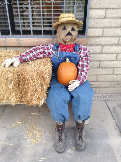 Scarecrow with red plaid shirt, bib overalls, and burlap face, sitting on a bale of straw, outdoors. I Love Fall! Scarecrow With Pumpkin Head, Sitting Scarecrow Diy, Diy Sitting Scarecrow, Horse Scarecrow, Face Sitting, Women’s Scarecrow Diy, Sitting Scarecrow, Full Size Scarecrow Wood, Halloween Window Display