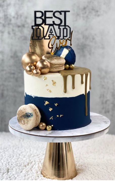 Blue and gold theme cake with the “Best Dad Ever” topper included. This regal cake is frosted with a white and rich dark blue buttercream and decorated with chocolate sails, macarons, golden balls and gold flakes. The Dads will love it! Rich Cake Design, Dark Blue And Gold Cake, Dark Blue Cake, Gold Theme Cake, Blue Gold Cake, Blue And Gold Cake, Fantasy Cakes, Fondant Cake Designs, Frosting Techniques