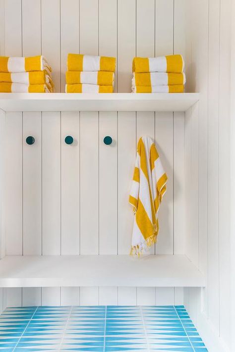 White and blue turquoise tiles lead to a white built-in bench fixed against vertical shiplap trim beneath peacock blue towel hooks. Poolhouse Bathroom, Chevron Floor Tile, Shiplap Trim, Pool House Cabana, Pool House Bathroom, Art Curation, Turquoise Tile, Herringbone Wallpaper, Custom Millwork