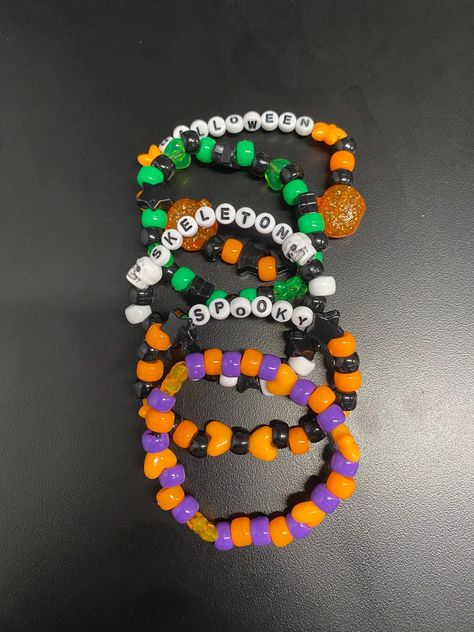 This Halloween-inspired Kandi bracelet set features vibrant, spooky designs perfect for the season. Each bracelet is crafted with colorful pony beads in classic Halloween hues like black, orange, purple, and neon green. Some bracelets might include fun themed charms like pumpkins, ghosts, bats, and skulls, while others could feature glow-in-the-dark or glittery beads for a magical touch. With playful patterns and festive flair, this set captures the eerie and whimsical spirit of Halloween, making it a fun accessory for raves, trick-or-treating, or costume parties. Halloween Kandi Ideas, Halloween Kandi Bracelets, Pony Bead Bracelets Patterns, Halloween Kandi, Kandi Charms, Purple And Neon Green, Bracelets Halloween, Kandi Inspiration, Pony Bead Jewelry